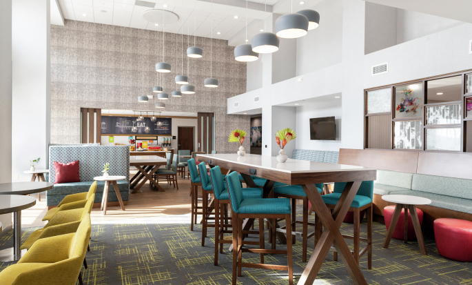 Lobby de un hotel Hampton by Hilton, con sillas y mesas para comer y trabajar.